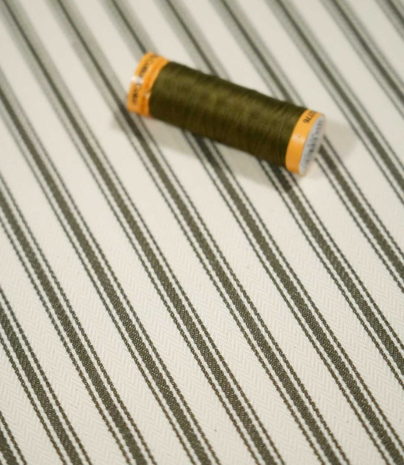 JF Ticking Forest striped fabric with coordinating green thread spool, highlighting the fine forest green stripes and ivory herringbone weave.