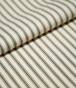 Folded JF Ticking Forest fabric showing its classic narrow forest green ticking stripe pattern on a warm ivory textured ground.