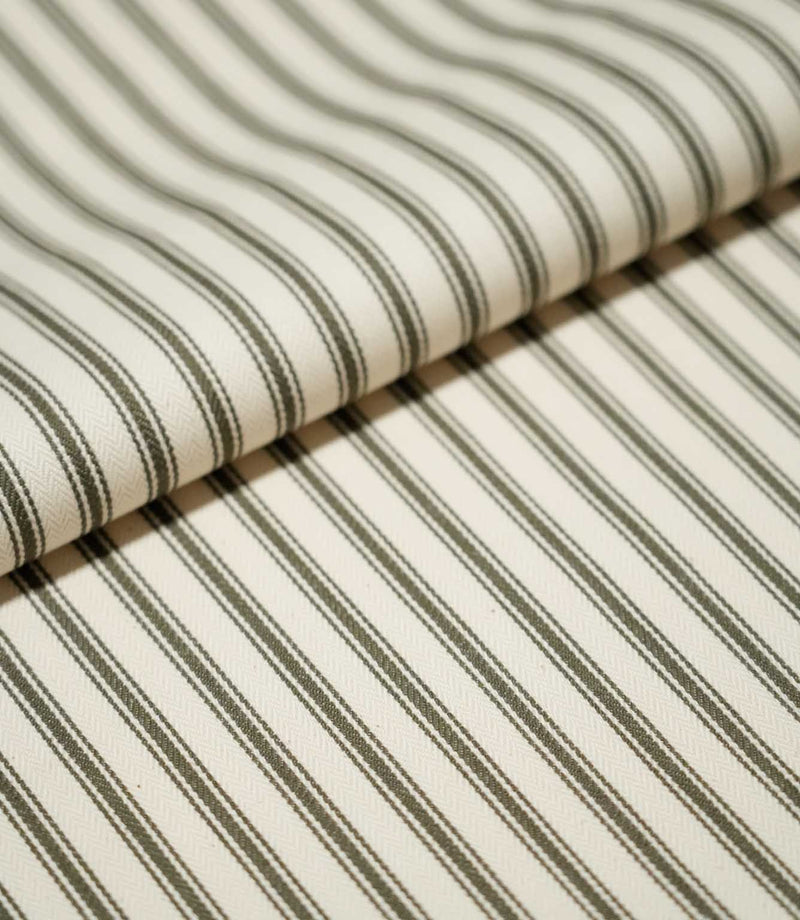 Folded JF Ticking Forest fabric showing its classic narrow forest green ticking stripe pattern on a warm ivory textured ground.