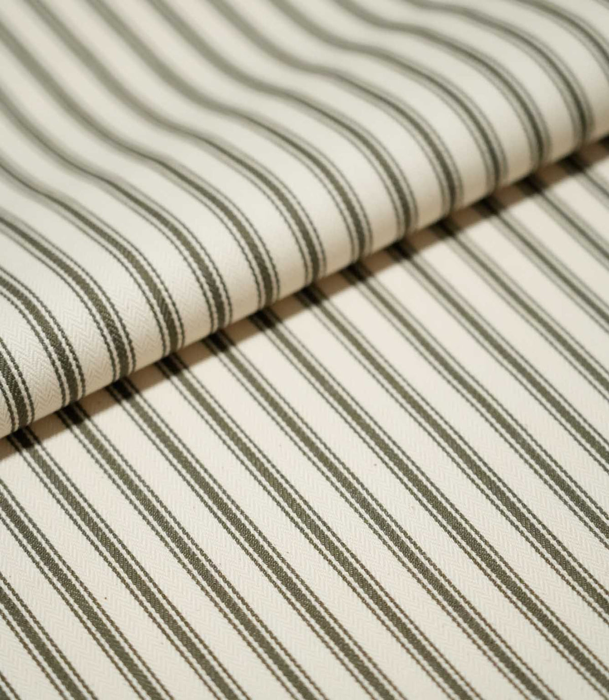 Folded JF Ticking Forest fabric showing its classic narrow forest green ticking stripe pattern on a warm ivory textured ground.