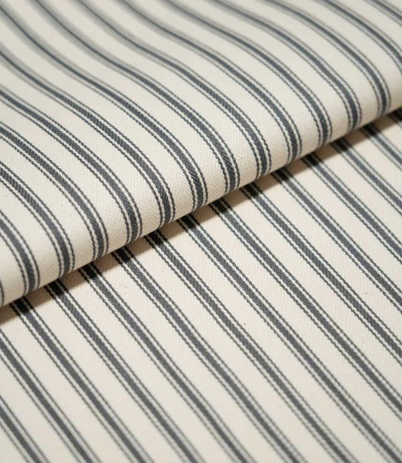 Close-up of folded JF Ticking Grey fabric showing the repeating charcoal grey ticking stripes and fine herringbone texture of the cream ground.