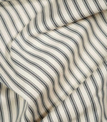 JF Ticking Grey fabric draped in soft folds, highlighting the natural drape, charcoal grey ticking stripes and subtle woven herringbone texture.
