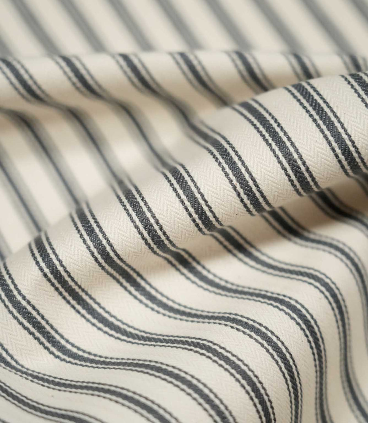 Detailed close-up of JF Ticking Grey fabric showing the charcoal grey woven ticking stripes, warm cream background and fine herringbone texture.