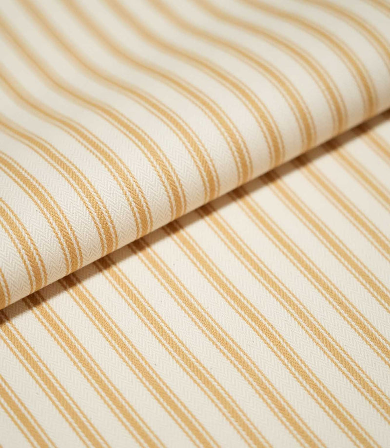 Close-up of folded JF Ticking Ochre fabric showing warm ochre ticking stripes against a cream ground with a subtle herringbone weave.