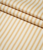 JF Ticking Ochre striped fabric arranged in layered folds, showing the repeating ochre stripe design and fine woven texture of the cream background.