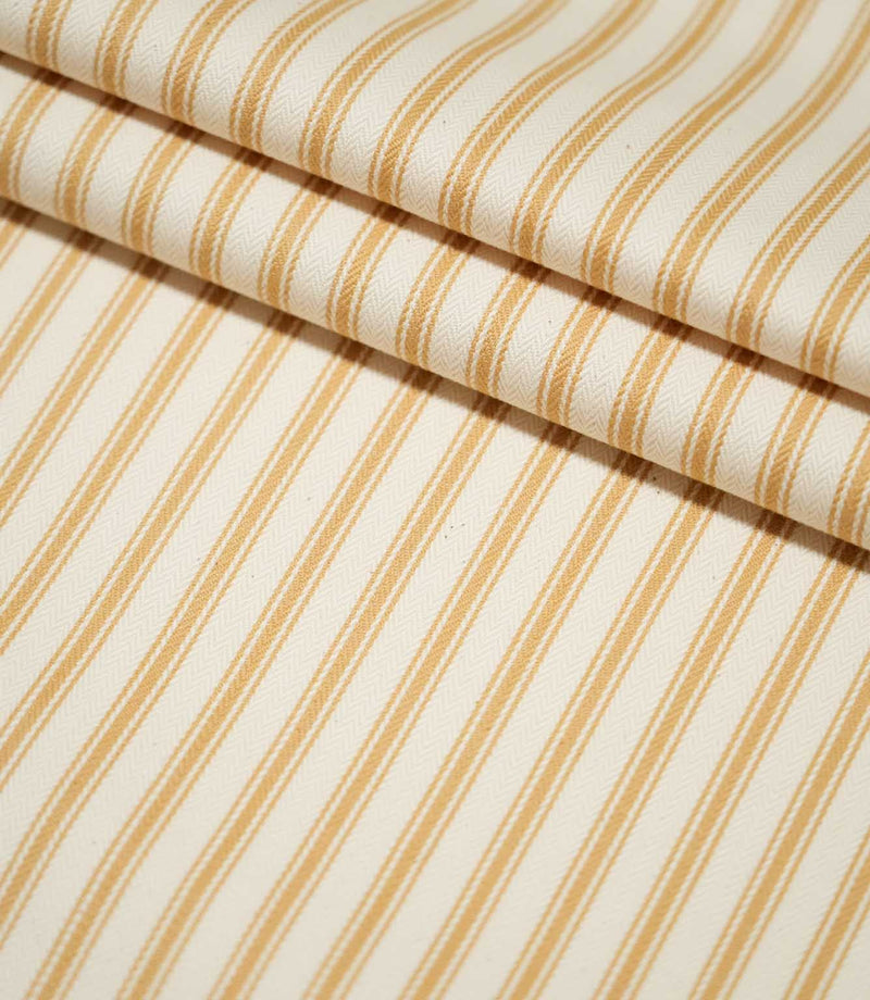 JF Ticking Ochre striped fabric arranged in layered folds, showing the repeating ochre stripe design and fine woven texture of the cream background.