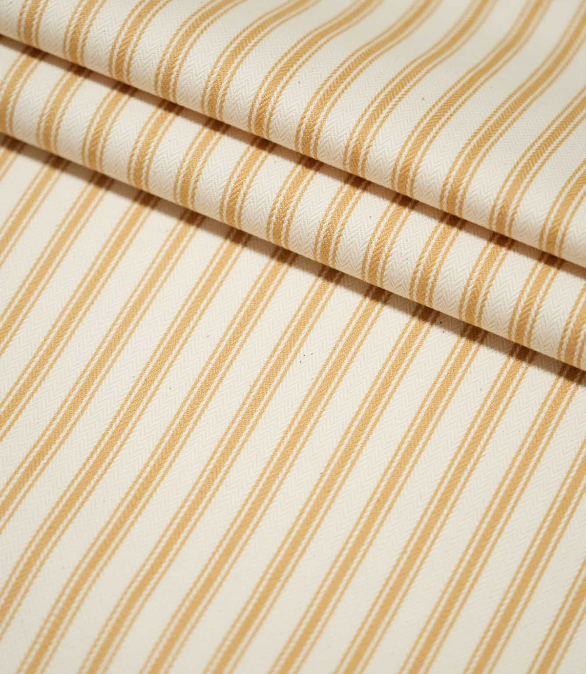 JF Ticking Ochre striped fabric arranged in layered folds, showing the repeating ochre stripe design and fine woven texture of the cream background.