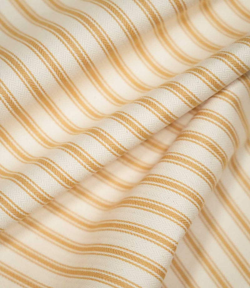 JF Ticking Ochre fabric draped in soft folds, highlighting the repeating ochre ticking stripes, cream background and natural movement of the fabric.