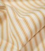 Detailed close-up of draped JF Ticking Ochre fabric showing the warm ochre double stripes and subtle herringbone texture of the cream woven ground.
