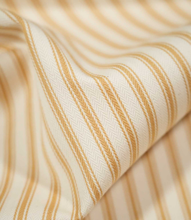 Detailed close-up of draped JF Ticking Ochre fabric showing the warm ochre double stripes and subtle herringbone texture of the cream woven ground.