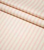 JF Ticking Pink fabric arranged in neat folds, showing the repeating soft pink ticking stripes and subtle woven herringbone texture.