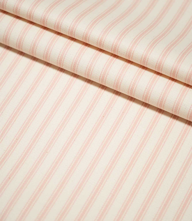JF Ticking Pink fabric arranged in neat folds, showing the repeating soft pink ticking stripes and subtle woven herringbone texture.