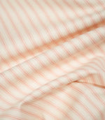 JF Ticking Pink fabric draped in soft folds, highlighting its natural drape, blush pink ticking stripe pattern and textured cream weave.