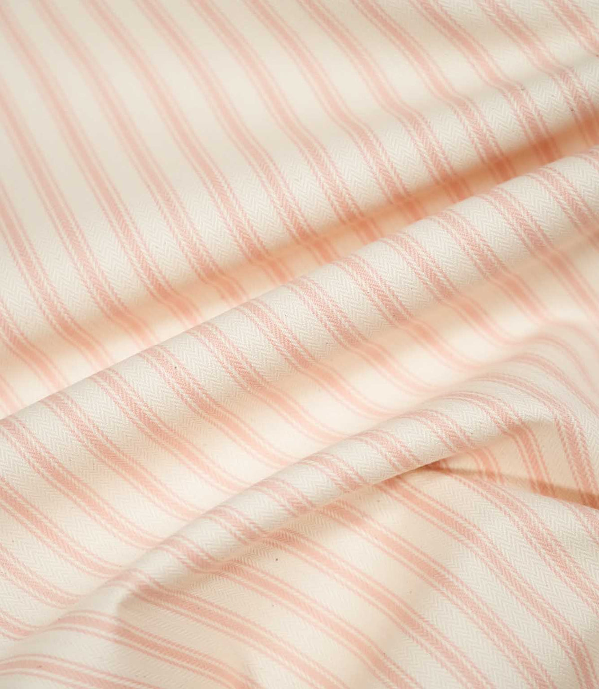 JF Ticking Pink fabric draped in soft folds, highlighting its natural drape, blush pink ticking stripe pattern and textured cream weave.
