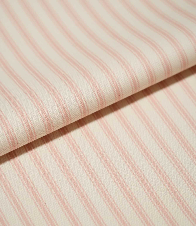 Close-up of folded JF Ticking Pink fabric showing soft pink ticking stripes and the fine herringbone texture of the cream woven ground.