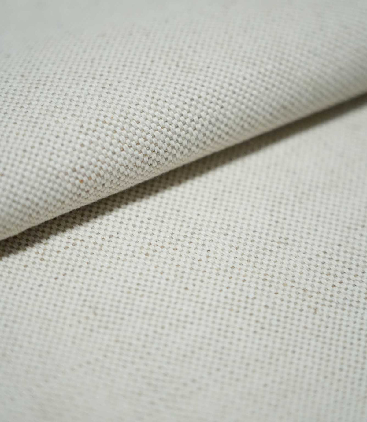 Close-up of JF Ticking Plain Natural fabric folded over itself, revealing its substantial woven texture, ivory cream colour and fine beige yarn detailing.