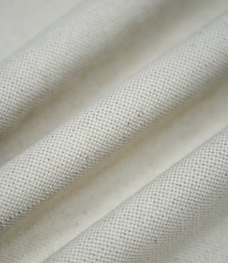 Detailed photograph of JF Ticking Plain Natural fabric draped into gentle folds, highlighting its structured weave, subtle beige flecks and natural ivory appearance.