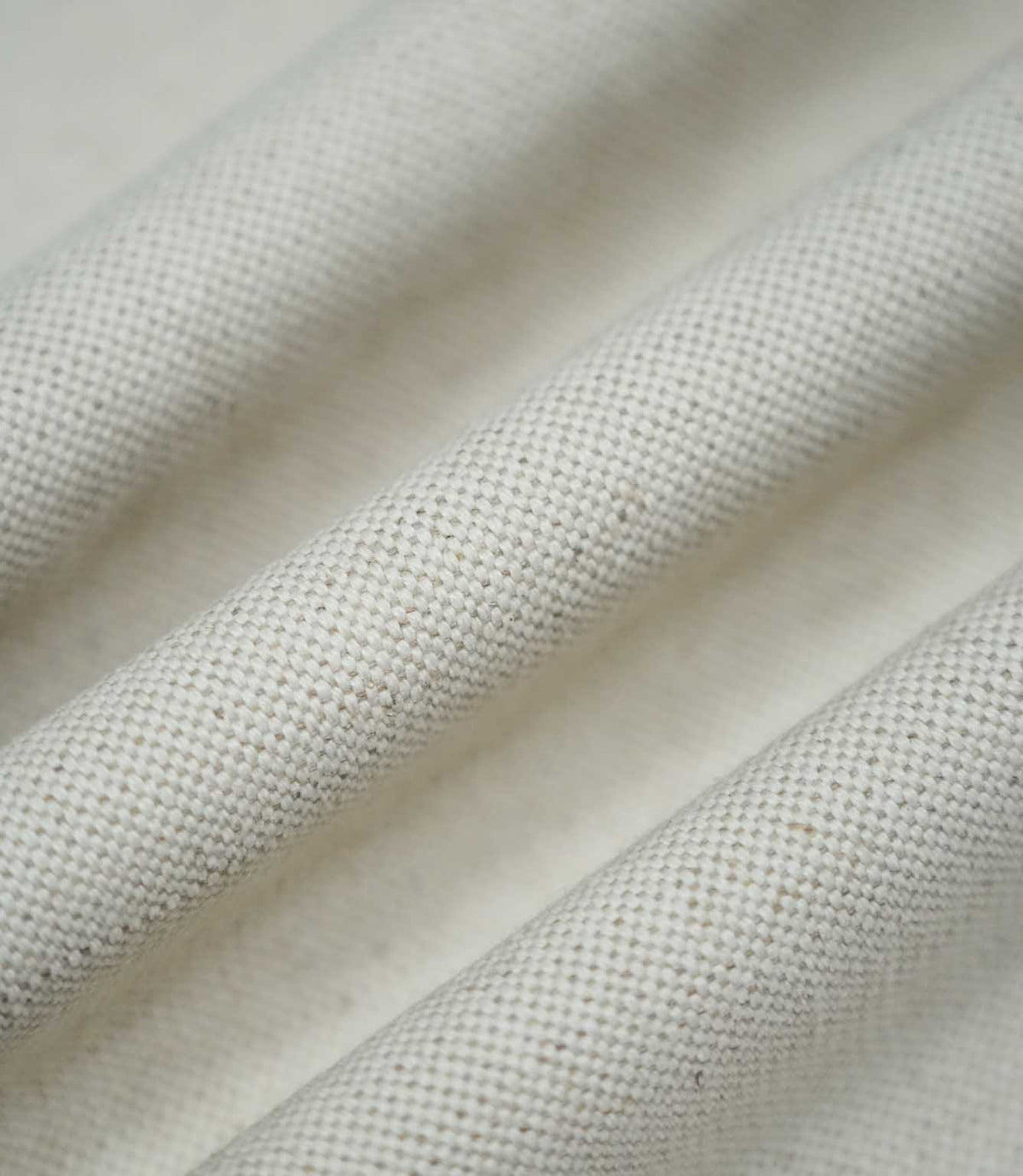 Detailed photograph of JF Ticking Plain Natural fabric draped into gentle folds, highlighting its structured weave, subtle beige flecks and natural ivory appearance.