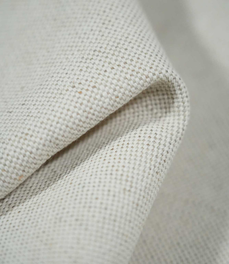 Macro photograph of JF Ticking Plain Natural fabric folded over itself, showing the thickness of the material, tightly interwoven cream yarns and natural textured finish.