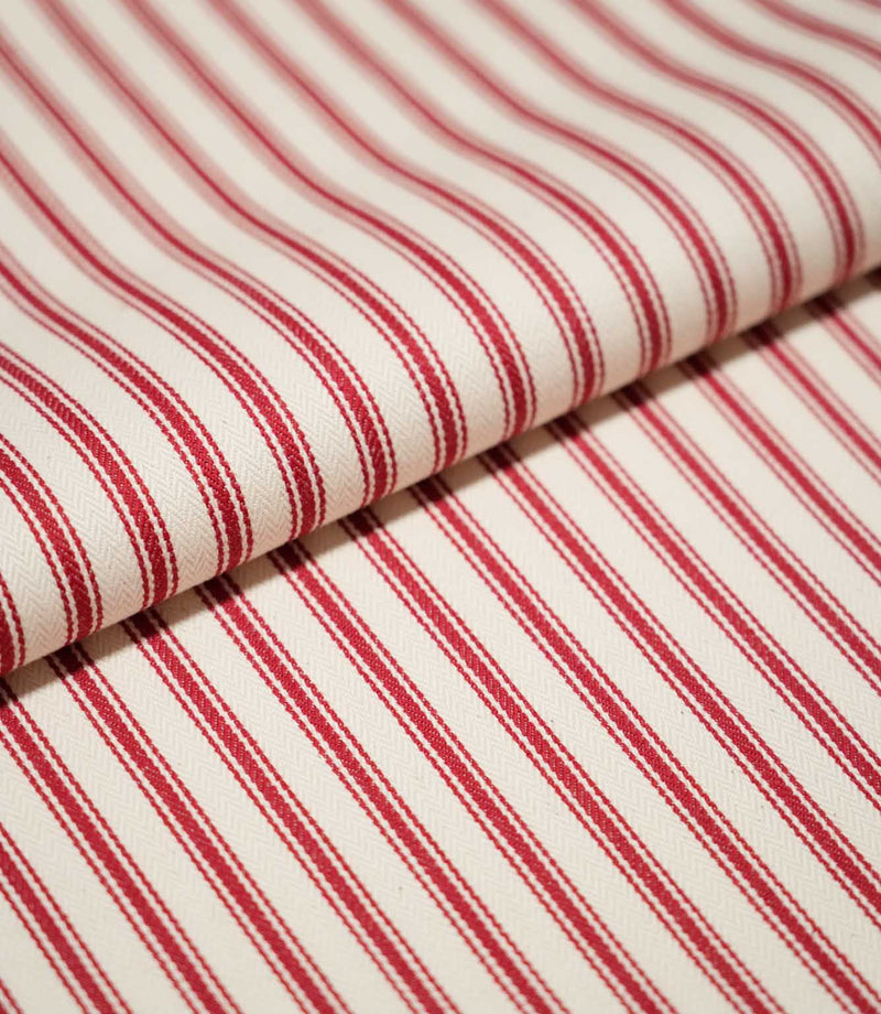 Close-up of folded JF Ticking Red fabric showing the repeating red ticking stripes and fine herringbone texture of the cream background.