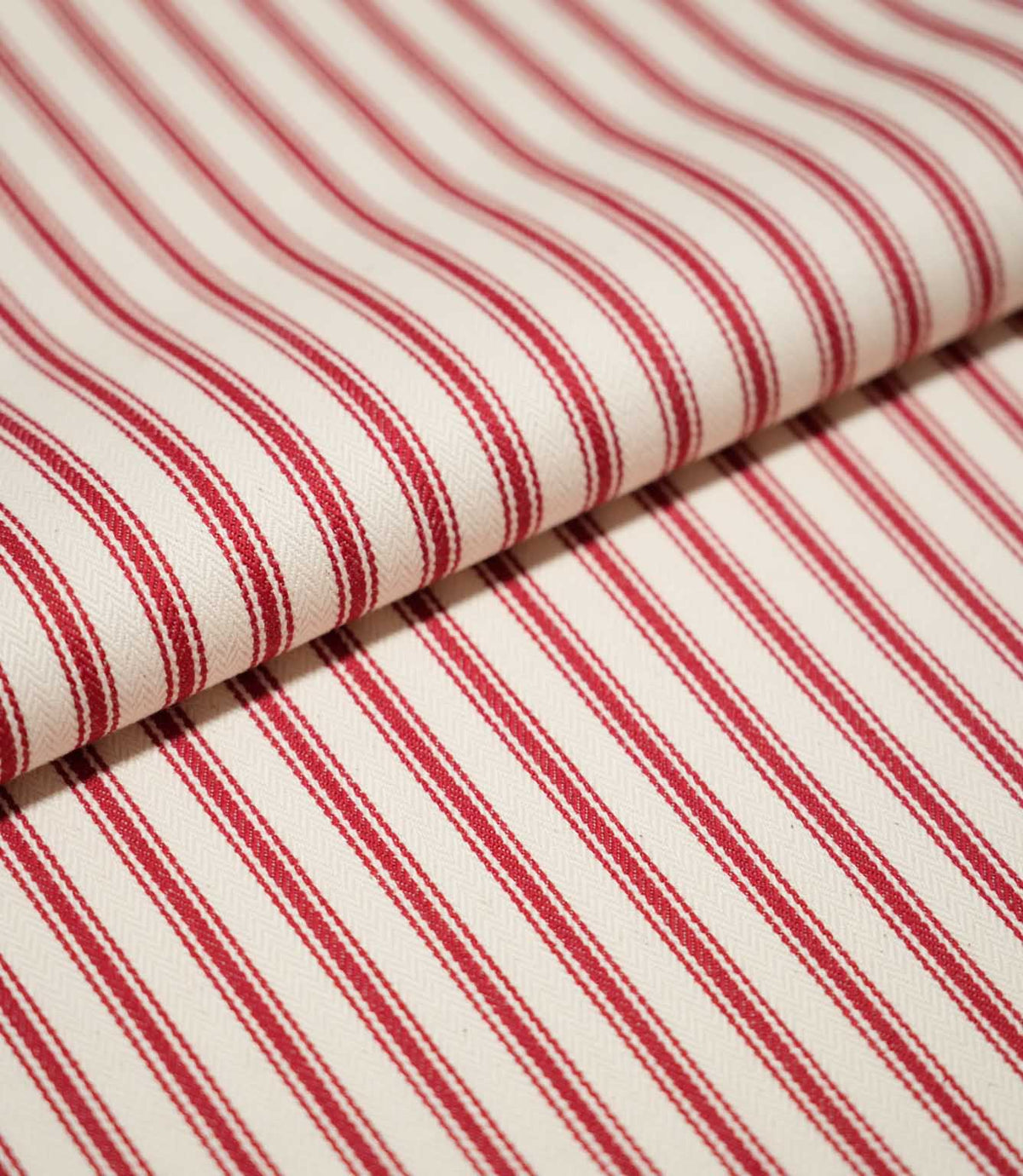 Close-up of folded JF Ticking Red fabric showing the repeating red ticking stripes and fine herringbone texture of the cream background.