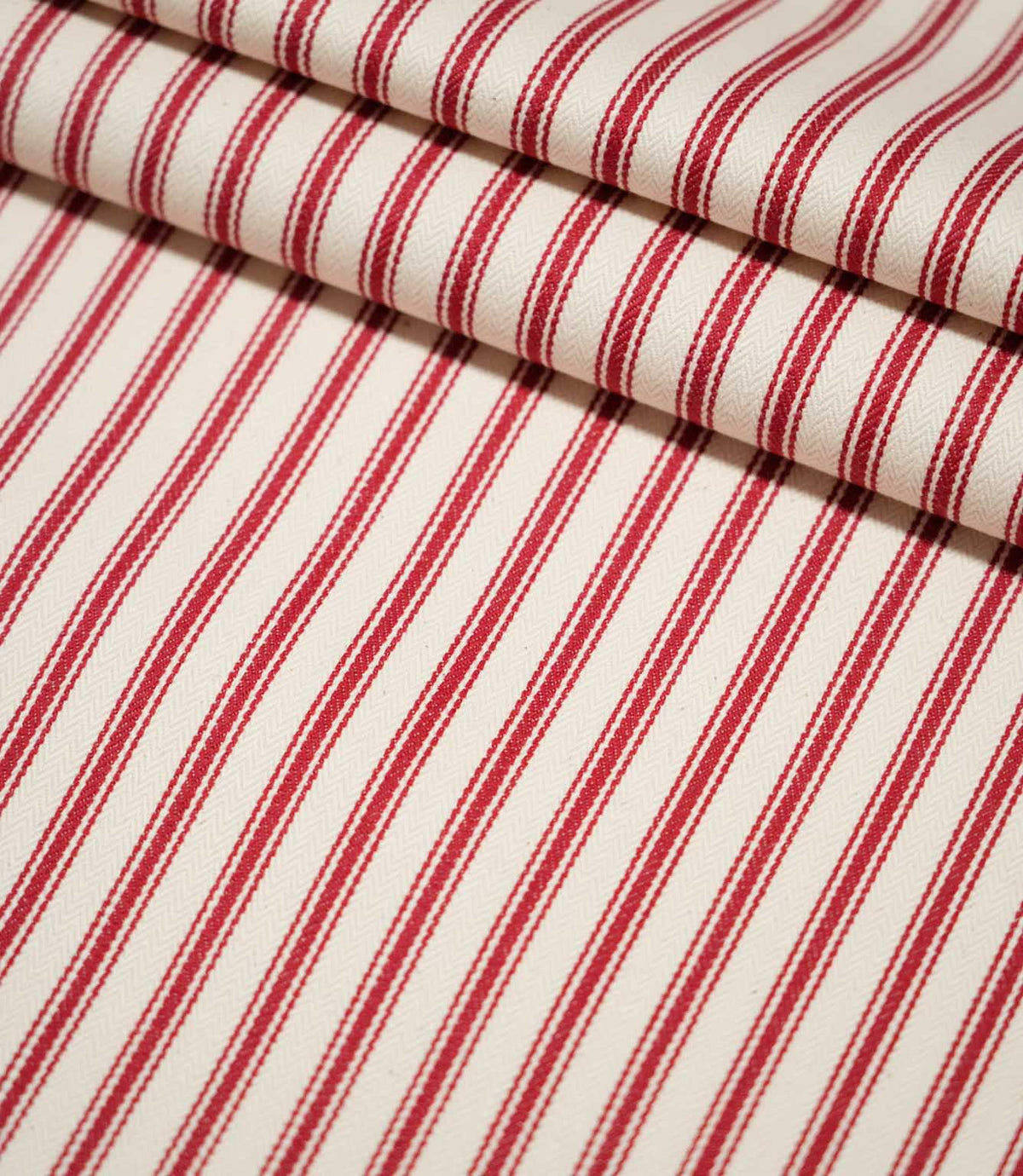 JF Ticking Red striped fabric arranged in neat folds, showing the bold repeating red stripes and textured cream herringbone weave.