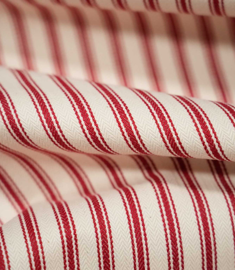 Detailed close-up of JF Ticking Red fabric showing the woven red ticking stripes and subtle herringbone texture against a warm cream background.