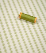 JF Ticking Sage Green fabric styled with a coordinating green thread spool, highlighting the striped design and subtle cream herringbone weave.