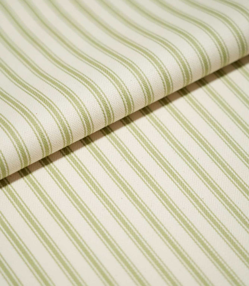 Close-up of folded JF Ticking Sage Green fabric showing the repeating sage green ticking stripes and fine herringbone texture of the cream background.