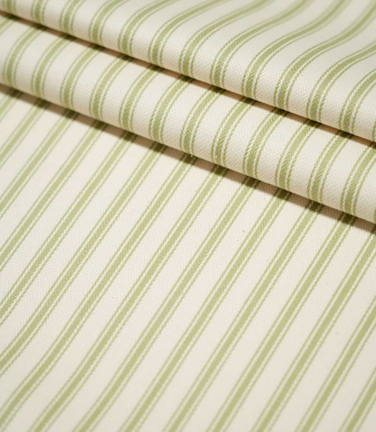 JF Ticking Sage Green striped fabric arranged in neat folds, showing the evenly spaced green stripes and textured cream herringbone weave.
