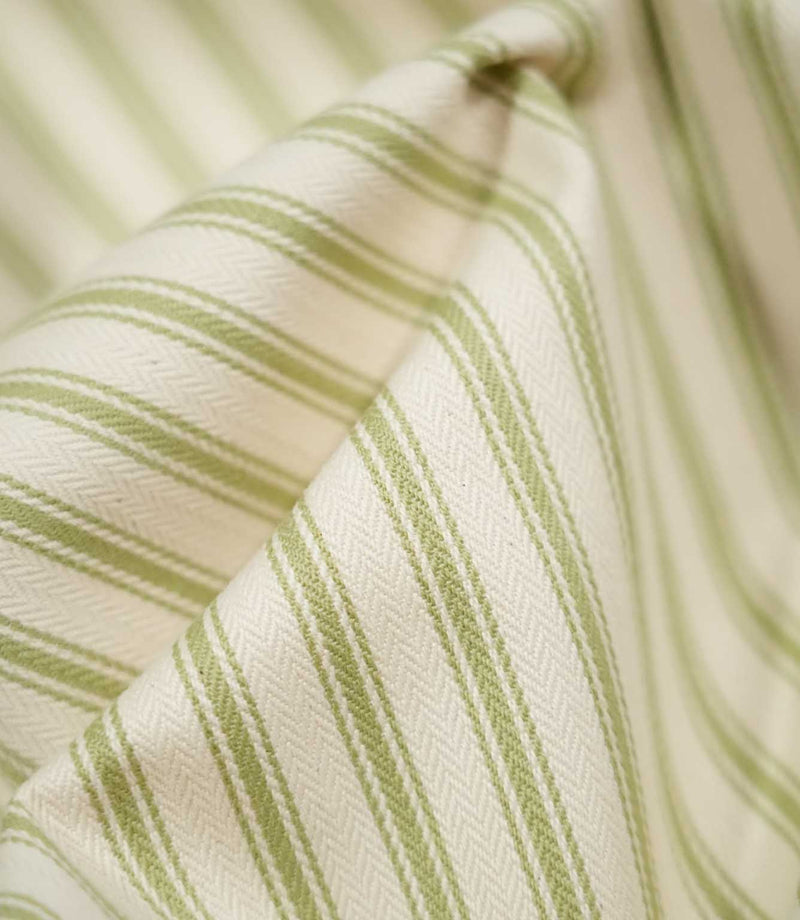 Detailed close-up of JF Ticking Sage Green fabric showing the woven green ticking stripes and subtle herringbone texture against a warm cream background.