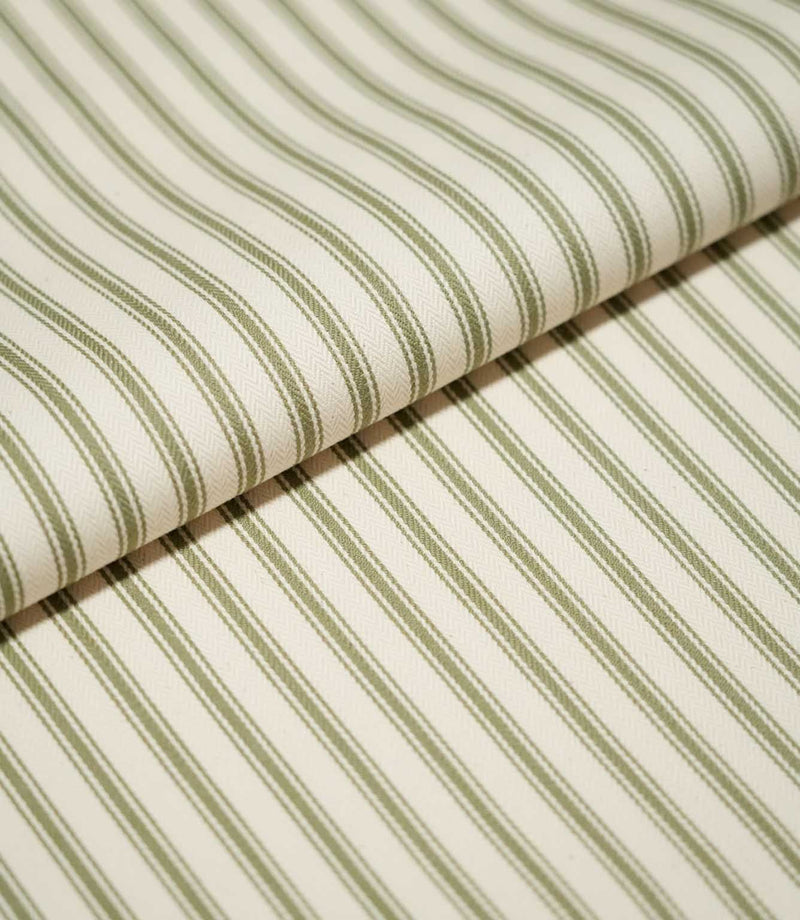 Close-up of folded JF Ticking Sap Green fabric showing the repeating olive green ticking stripes and fine woven herringbone texture of the cream background.