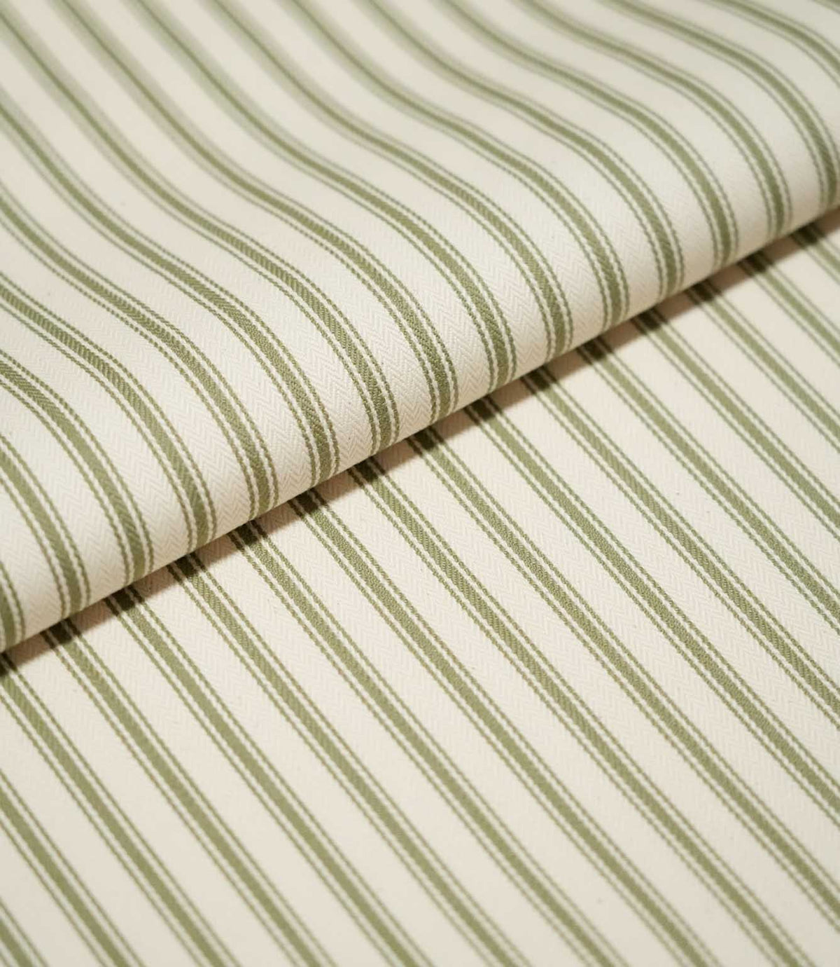 Close-up of folded JF Ticking Sap Green fabric showing the repeating olive green ticking stripes and fine woven herringbone texture of the cream background.