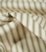 Detailed close-up of JF Ticking Sap Green fabric showing olive green woven ticking stripes, a warm cream background and subtle herringbone texture.