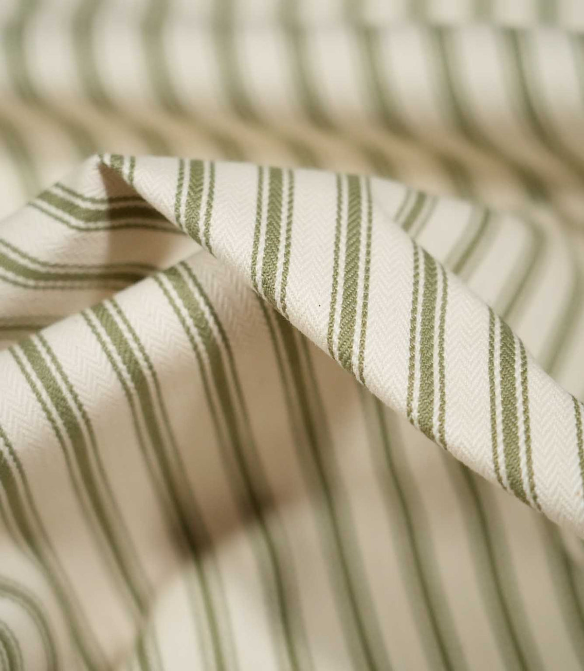 Detailed close-up of JF Ticking Sap Green fabric showing olive green woven ticking stripes, a warm cream background and subtle herringbone texture.