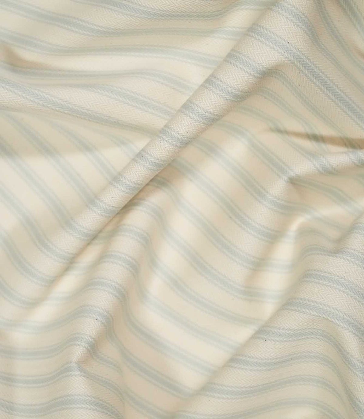 JF Ticking Seaspray fabric draped in soft folds, showing the pale blue ticking stripe pattern, cream ground and natural movement of the woven fabric.