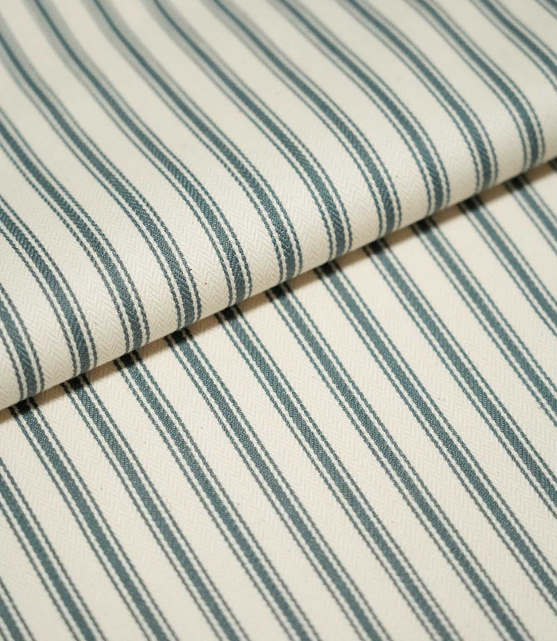 Close-up of folded JF Ticking Teal fabric showing dark teal ticking stripes against a cream ground with a subtle herringbone weave.