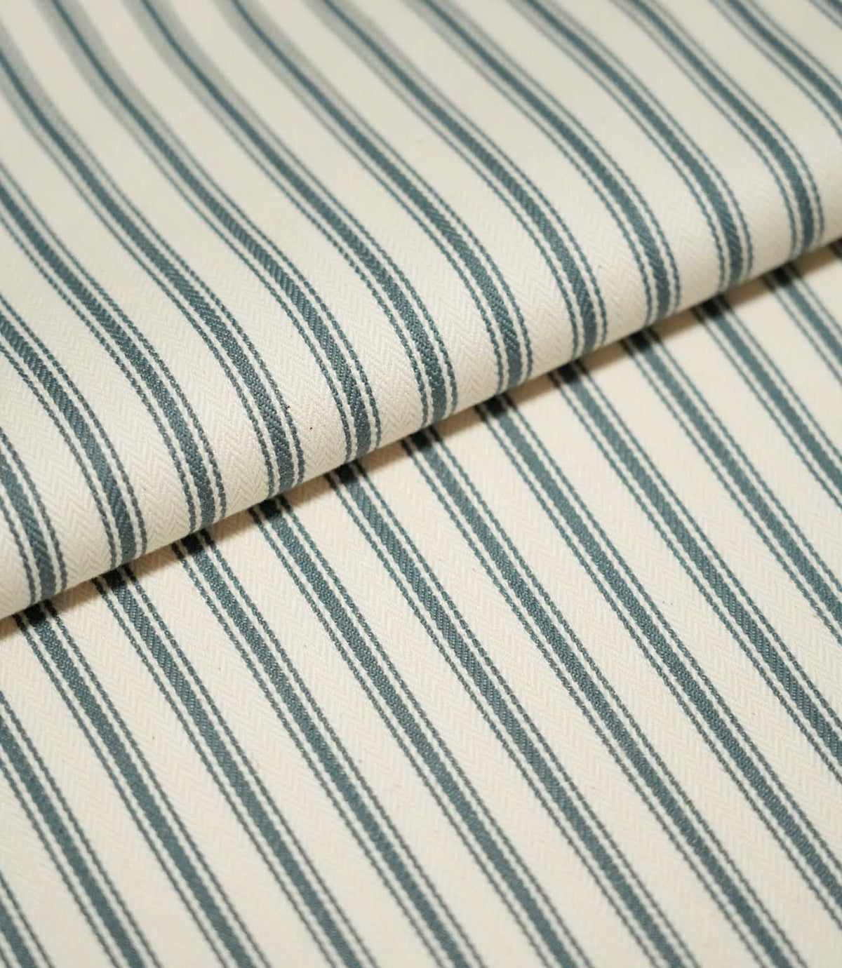 Close-up of folded JF Ticking Teal fabric showing dark teal ticking stripes against a cream ground with a subtle herringbone weave.