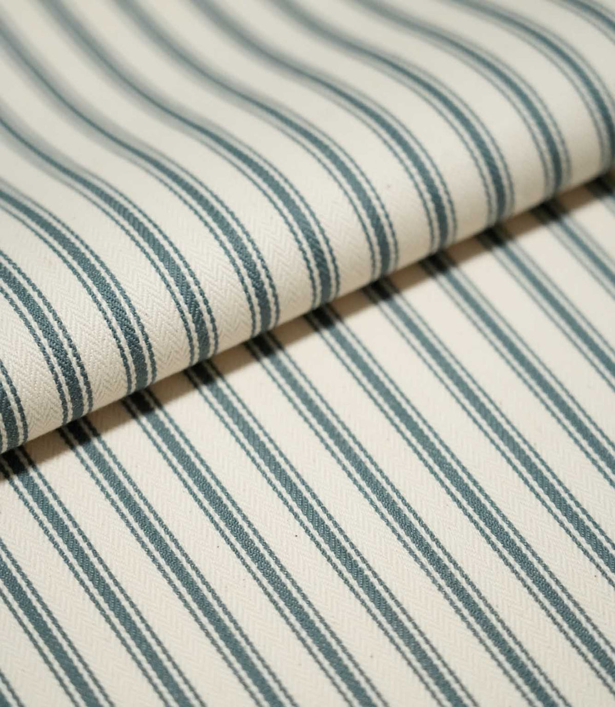 Detailed close-up of JF Ticking Teal striped fabric arranged in a soft fold, highlighting the repeating teal stripes and fine woven herringbone texture.