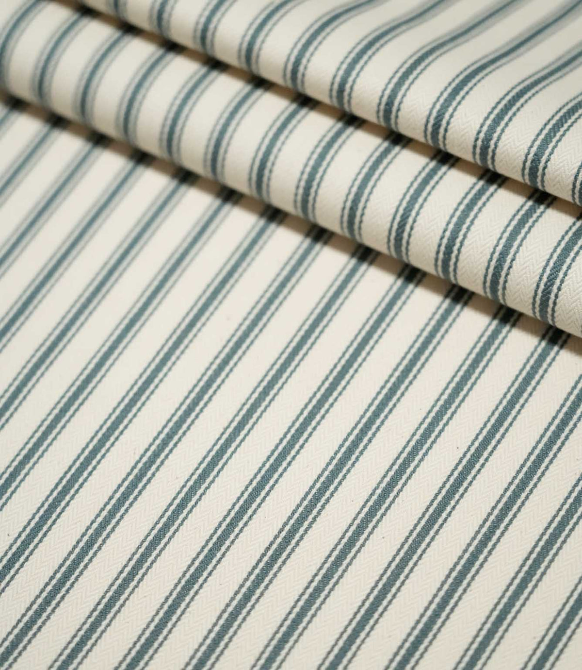 JF Ticking Teal fabric arranged in layered folds, showing the repeating dark teal ticking stripe pattern across the cream woven background.