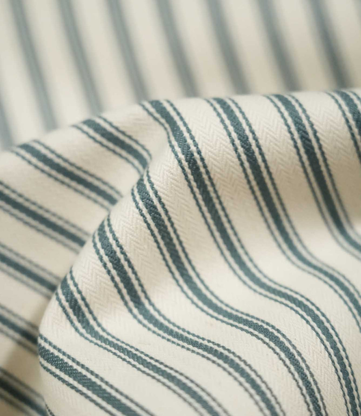 Close-up of draped JF Ticking Teal fabric highlighting the dark teal double stripes, cream ground and subtle herringbone woven texture.