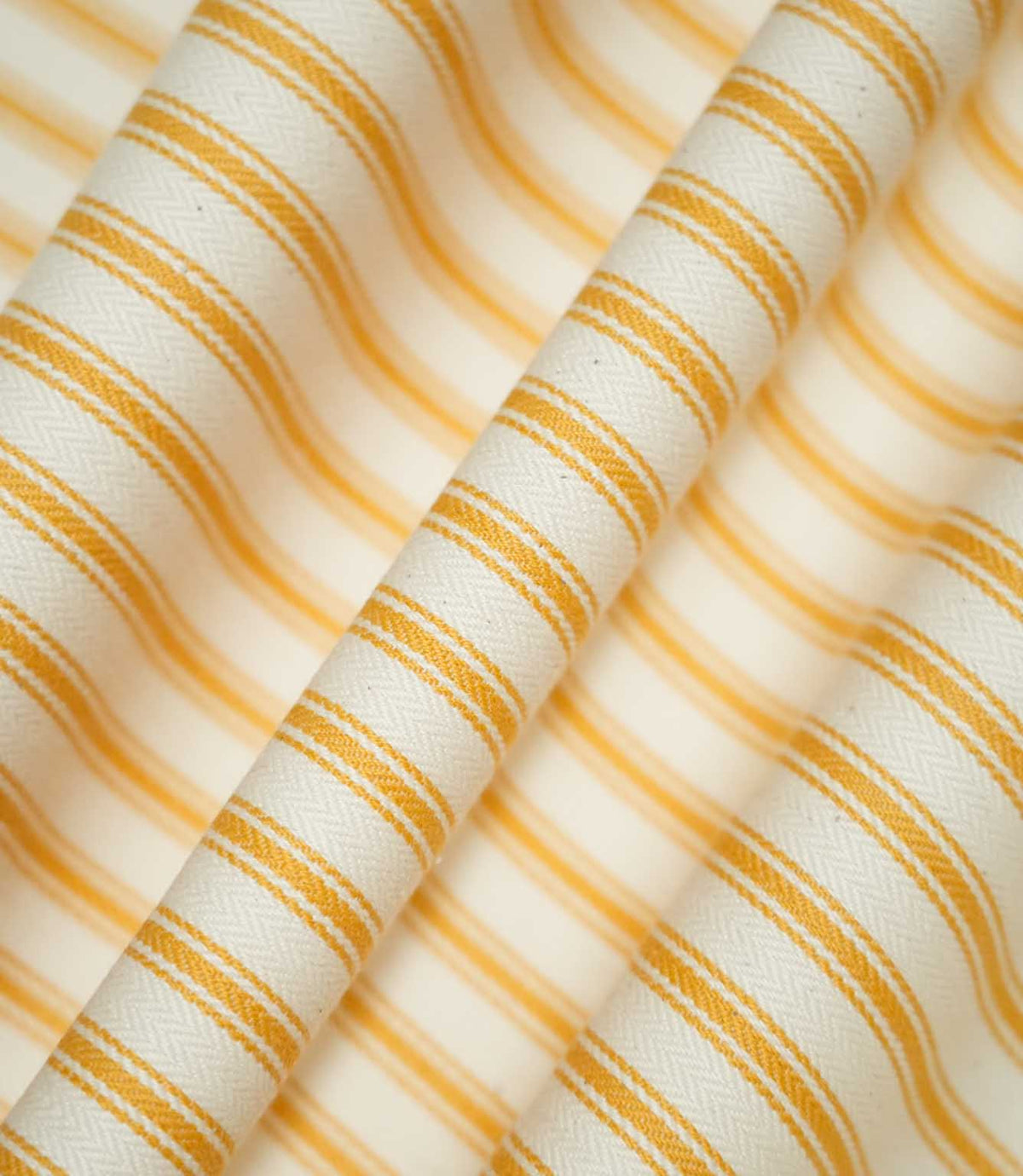 JF Ticking Turmeric striped fabric draped into soft, flowing folds, displaying the classic turmeric yellow and cream ticking stripe design and subtle herringbone texture.