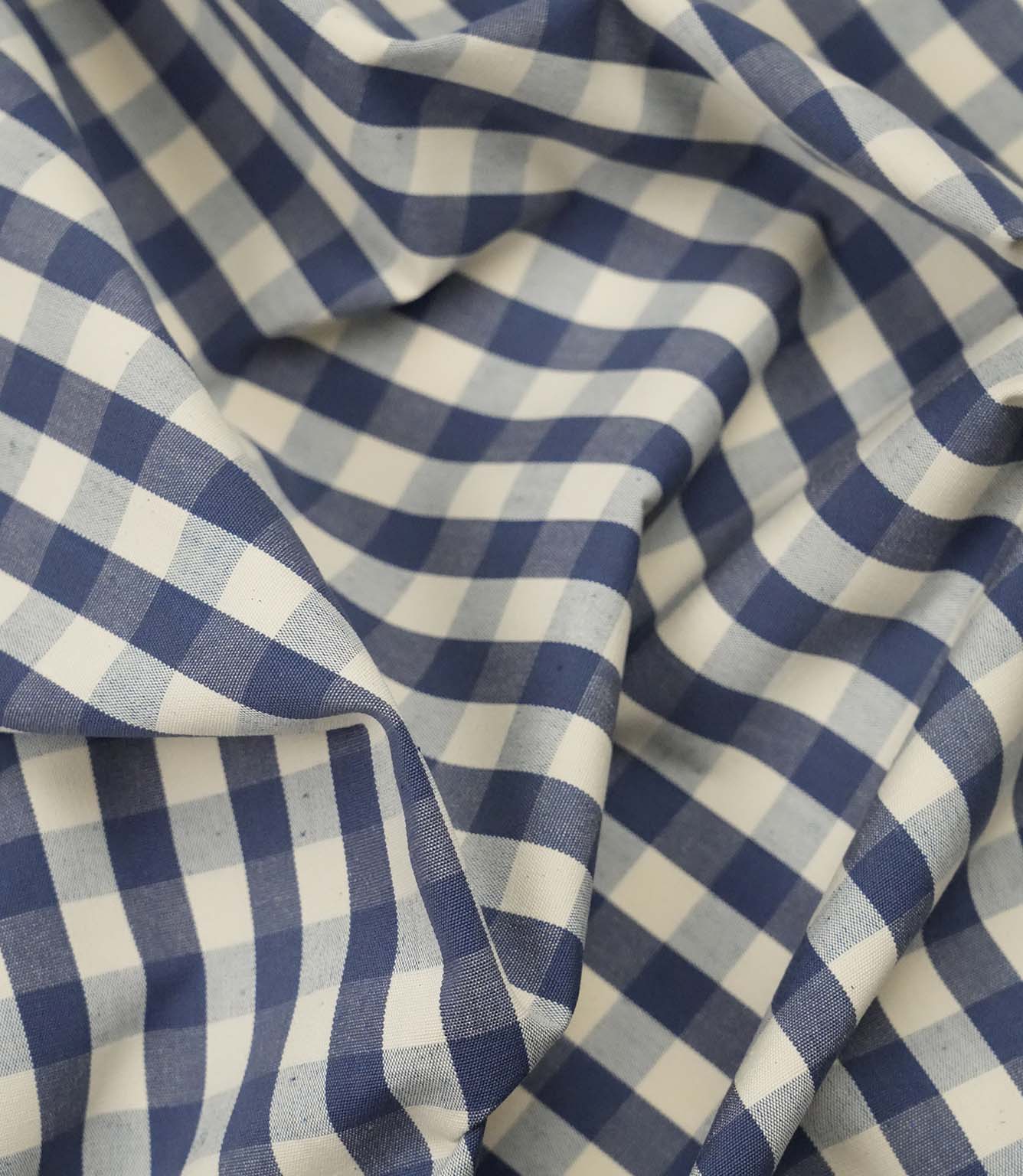 Blue and ivory gingham fabric draped to show its soft handle and classic checked design for interiors and sewing.
