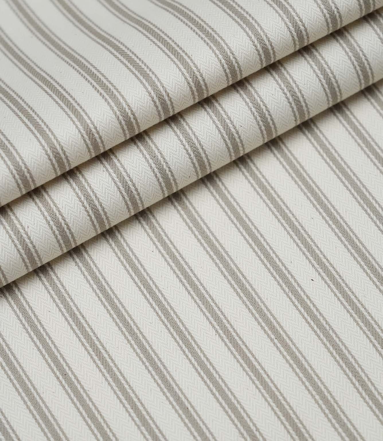 Layered folds of beige ticking stripe fabric displaying the fine herringbone weave and timeless striped pattern.
