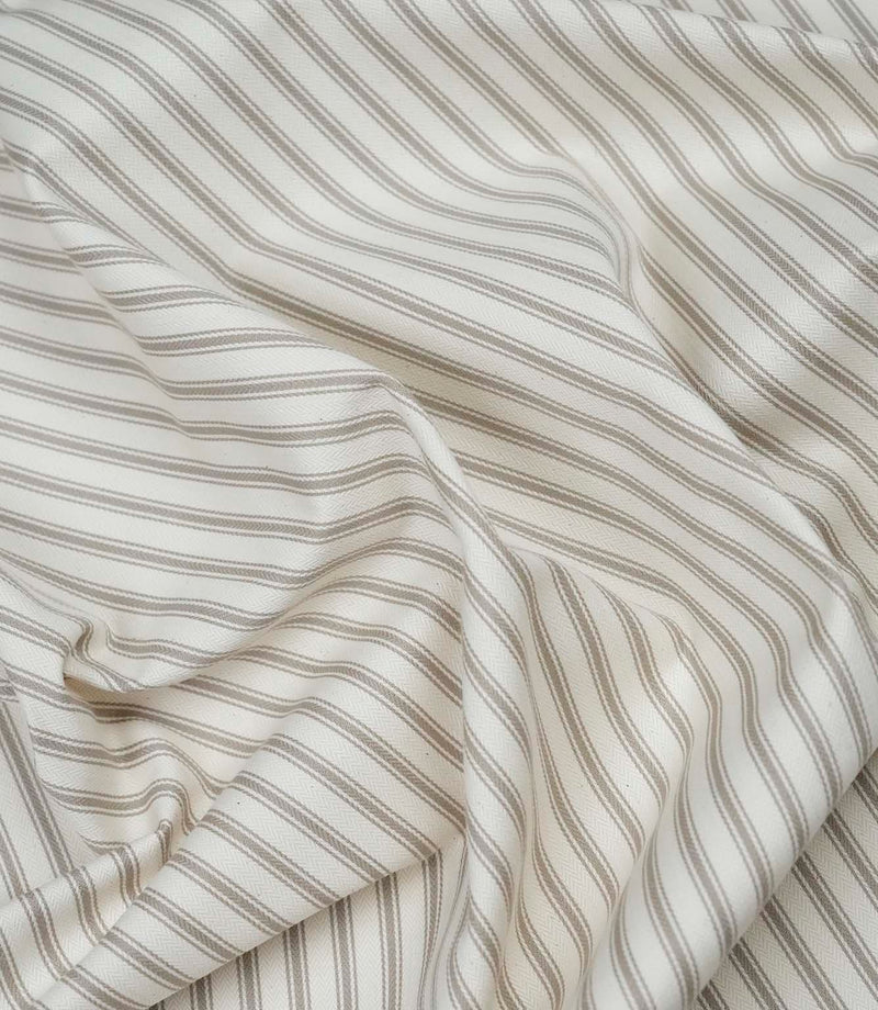 Beige ticking stripe fabric draped to show its soft handle, classic stripe design and subtle herringbone texture.