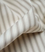 Close-up detail of beige ticking stripe fabric showing the fine woven texture and classic neutral stripe pattern.