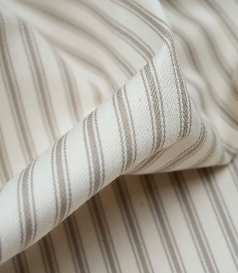 Close-up detail of beige ticking stripe fabric showing the fine woven texture and classic neutral stripe pattern.