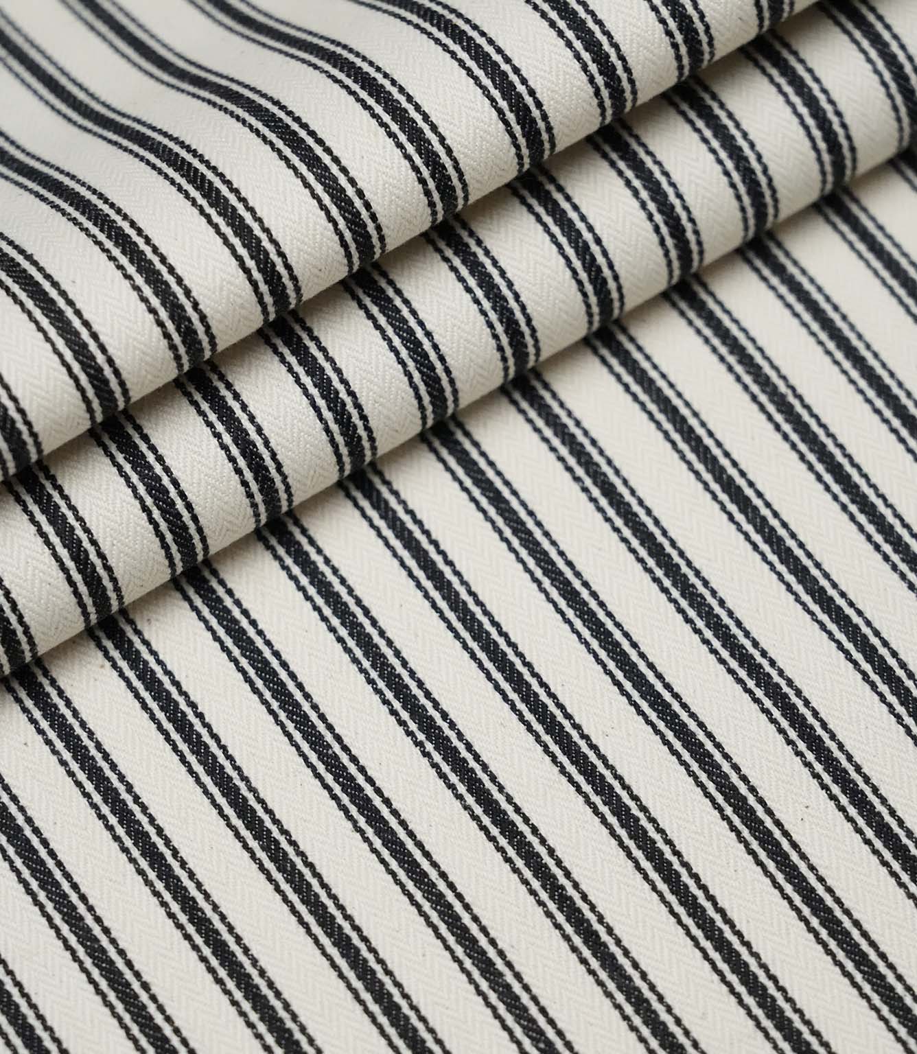 Layered folds of black ticking stripe fabric displaying the fine herringbone weave and classic striped design.