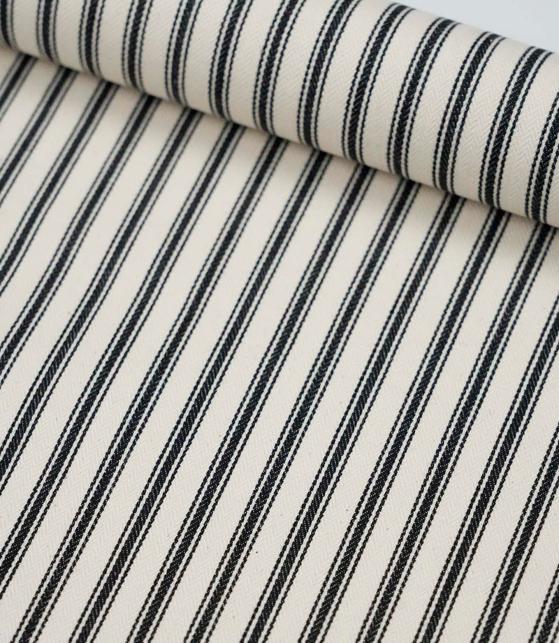 Rolled black ticking stripe fabric highlighting the bold monochrome stripes and subtle woven texture.
