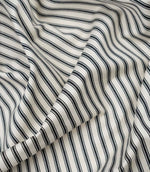 Black ticking stripe fabric draped to show its soft handle, classic stripe pattern and woven herringbone texture.
